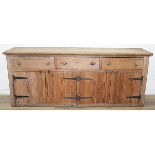 61 - A large antique pine dresser base comprising of three deep drawers with turned handles over four cup... 