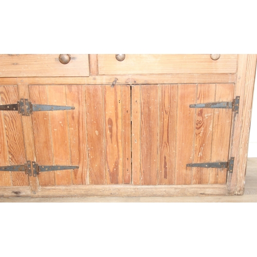 61 - A large antique pine dresser base comprising of three deep drawers with turned handles over four cup... 