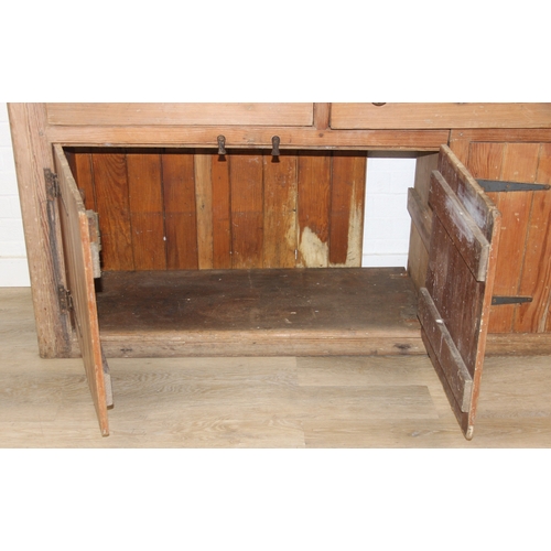 61 - A large antique pine dresser base comprising of three deep drawers with turned handles over four cup... 