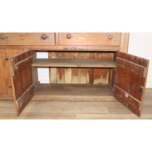 61 - A large antique pine dresser base comprising of three deep drawers with turned handles over four cup... 