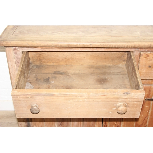 61 - A large antique pine dresser base comprising of three deep drawers with turned handles over four cup... 