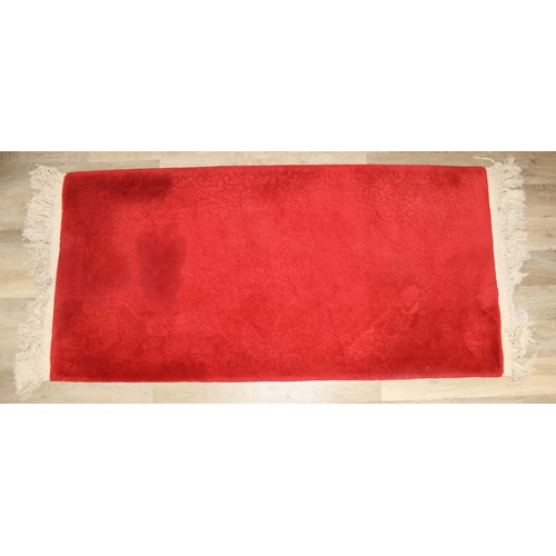 210 - A red ground rug with floral decoration, one of two in the sale, 209cm x 94cm