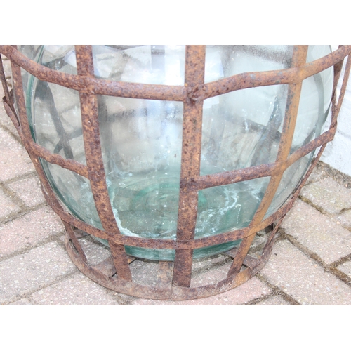 313 - A large vintage glass carboy in iron basket, 52cm in diameter x 62cm tall
