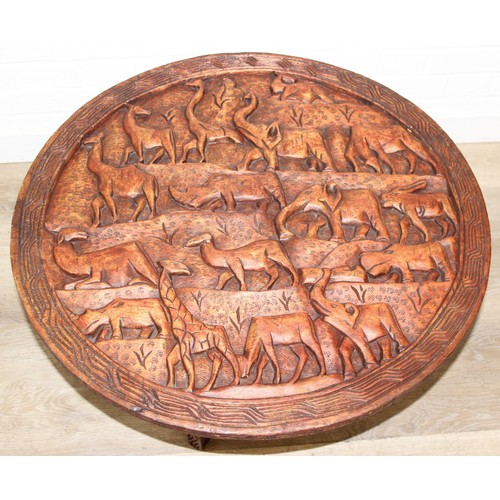 66 - Three African carved hardwood folding tables, the tops carved with elephants, rhinos, giraffes etc, ... 