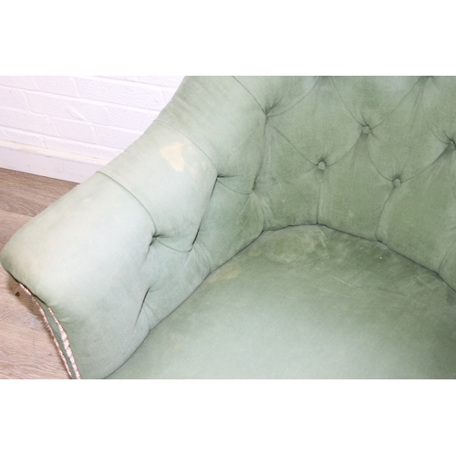 97 - An antique green upholstered tub chair with button backed upholstery, turned wooden legs and brass a... 