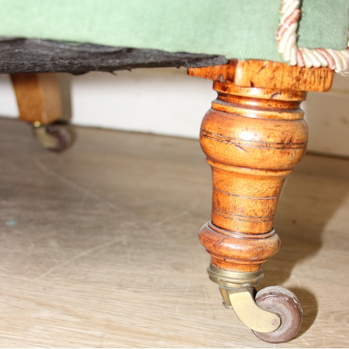 97 - An antique green upholstered tub chair with button backed upholstery, turned wooden legs and brass a... 