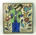A Persian pottery tile, possibly 18th century, painted with a woman in a garden holding a flagon and... 