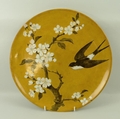 A Mintons charger, decorated with white blossom and a swallow on a mustard coloured ground, stamped ... 