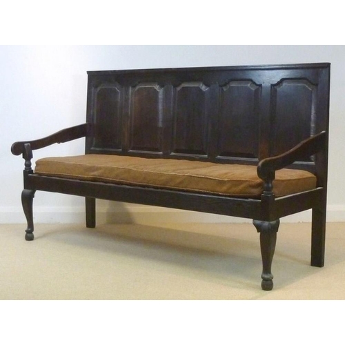 658 - A 18th century oak long settle, with five fielded panel back rest, shaped open arms, raised on cabri... 