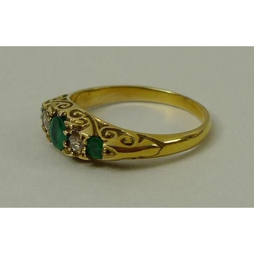 809 - An emerald and diamond five stone ring with three emeralds, interspersed with two diamonds within sc... 