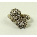A diamond crossover ring, circa 1930, formed as two flowers with central stone surrounded by seven s... 