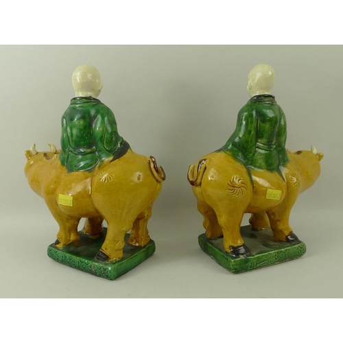 526 - A pair of earthenware Tang style figurines, each depicting a Buddhist figure riding an ox, in green ... 