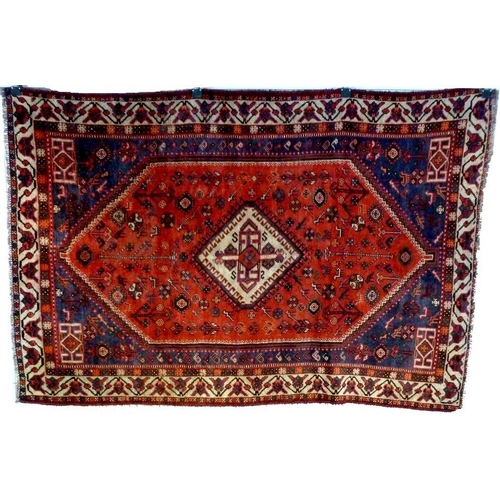 1050A - A Shiraz rug with orange red ground, central cream diamond medallion with latchhook decoration, dark... 