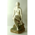 A Royal Dux Bohemia porcelain figure, early 20th century, of a nude young woman, sitting on moss cov... 