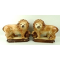 A pair of Staffordshire pottery lions, 19th century, each with glass bead eyes, with raised paw on b... 