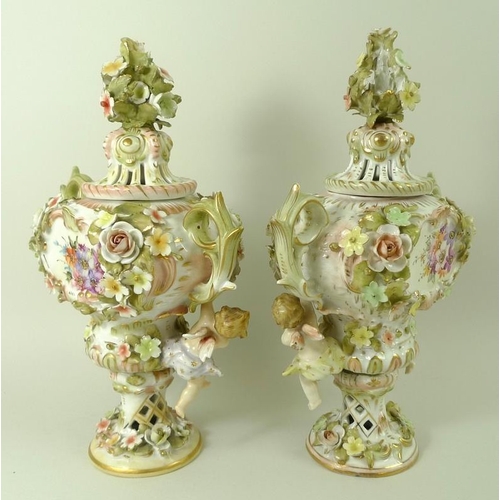 557 - A pair of Sitzendorf lidded vases, decorated in high relief with flowers and pair of putti, with pie... 