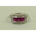 An 18ct white gold, ruby and diamond ring, with three central square cut rubies surrounded in a rect... 