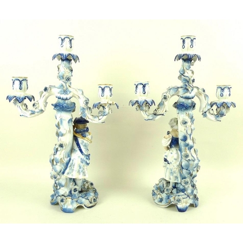 559 - A pair of Sitzendorf porcelain figural three-branch candlesticks, early 20th century, one modelled a... 