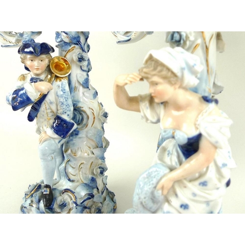 559 - A pair of Sitzendorf porcelain figural three-branch candlesticks, early 20th century, one modelled a... 