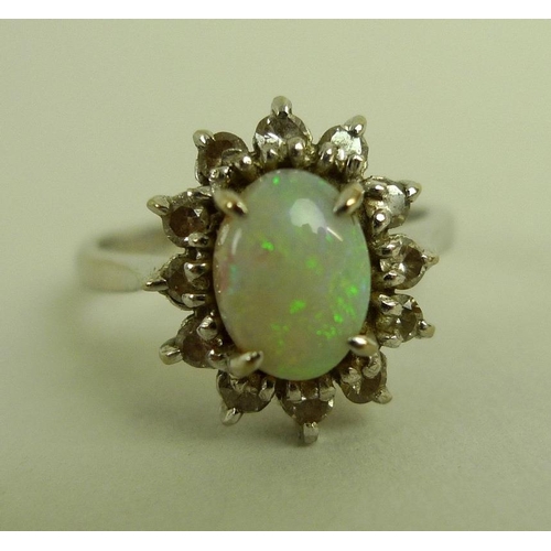 838 - An 18ct white gold and opal dress ring, the central oval cabochon cut opal surrounded by twelve diam... 