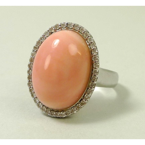 876 - A coral and diamond ring, the oval angel pink cabochon within a surround of brilliant cut diamonds, ... 