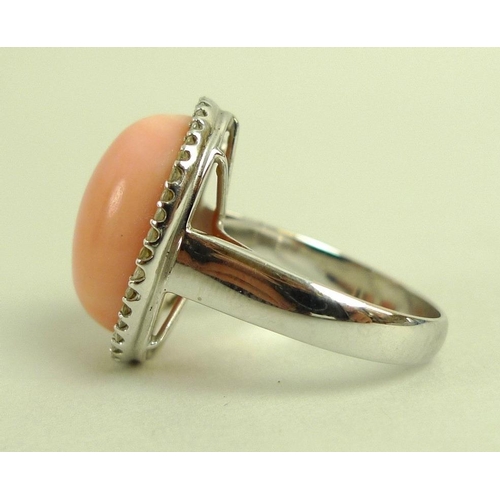 876 - A coral and diamond ring, the oval angel pink cabochon within a surround of brilliant cut diamonds, ... 