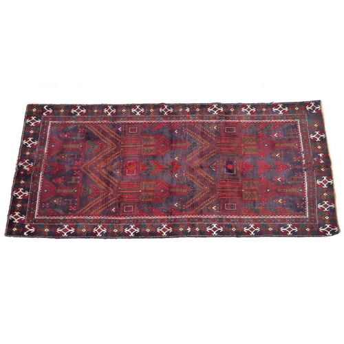 932 - A Baluchi rug with red ground, dark coloured geometric patterned field, white and orange cross motif... 