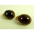 A pair of early 20th century gold cufflinks, set with red hard stone oval cabochons, likely garnet, ... 