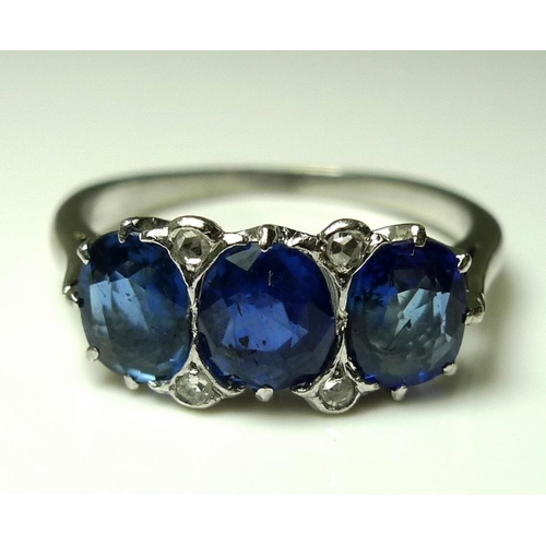 834 - A platinum and sapphire three stone ring, the central stone off-set with four diamonds, each sapphir... 