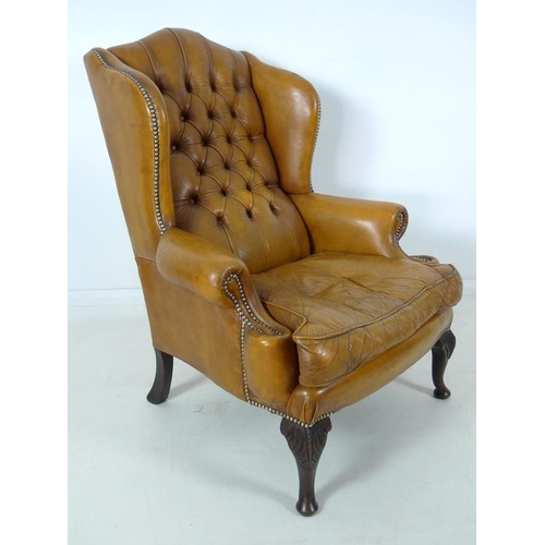 876 - A Georgian style tan button back leather arm chair, scroll over arms, brass tacks, carved front supp... 