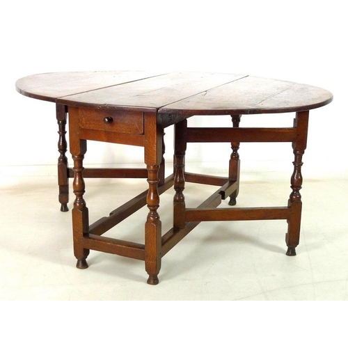 923 - A Georgian oak drop leaf table, oval surface, kick legs, turned supports and stretchers, 115 by 46.5... 