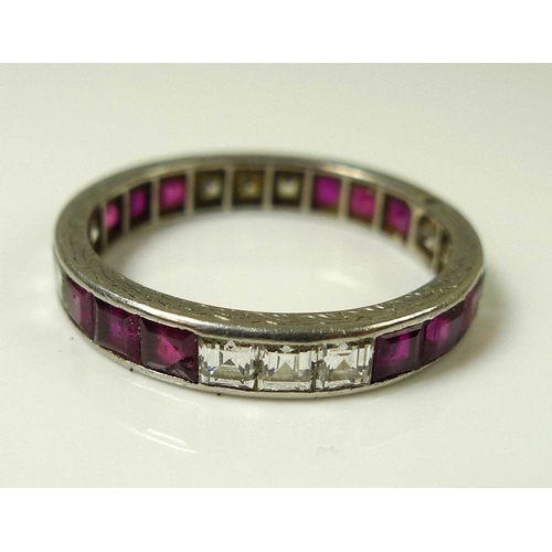 845 - A white gold, ruby and diamond eternity ring, the scroll engraved band set with twelve emerald cut d... 