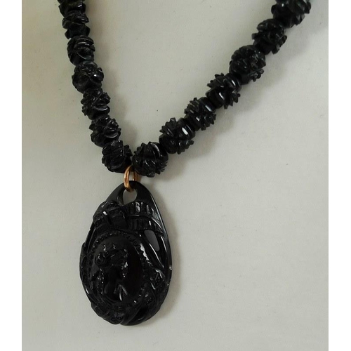 880 - A Whitby jet necklace, the tear drop shaped pendant relief carved with a lady's head in profile and ... 