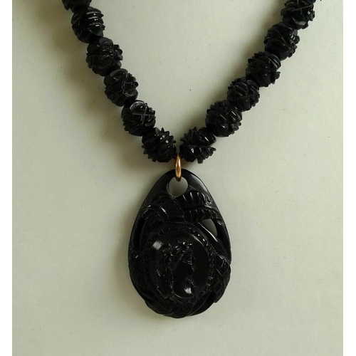 880 - A Whitby jet necklace, the tear drop shaped pendant relief carved with a lady's head in profile and ... 