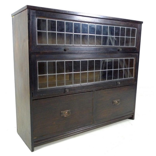 941 - A mid 20th century stained oak bookcase, with two full width slide and hide leaded glass doors, over... 