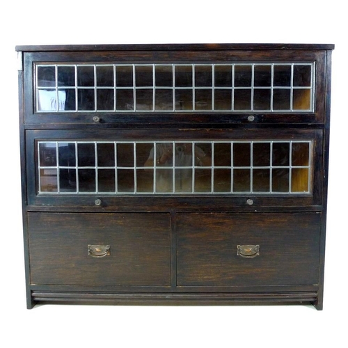 941 - A mid 20th century stained oak bookcase, with two full width slide and hide leaded glass doors, over... 