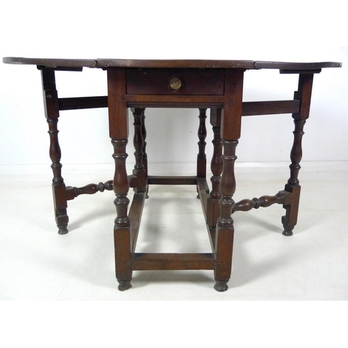 994 - An 18th century oak drop leaf table, oval surface, single drawer with brass knob, turned supports wi... 