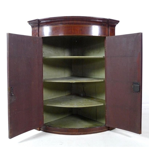 995 - An early Victorian bowfront mahogany and line inlaid corner cupboard, twin doors enclosing three fix... 