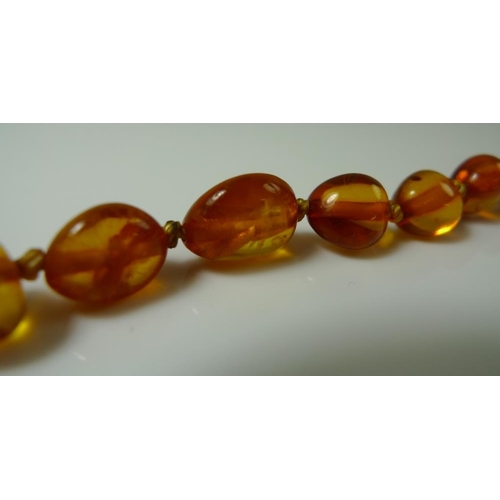 901 - An amber bead necklace, the oval beads each approximately 8mm with larger central bead of 11mm, whit... 