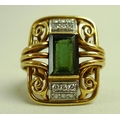 An 18ct gold dress ring, set with a dark green emerald cut stone flanked by twelve diamonds, the yel... 
