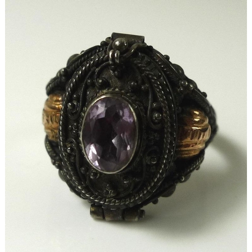 811 - An early 20th century silver poison ring, the hinged lid set with oval amethyst, applied bead and fo... 