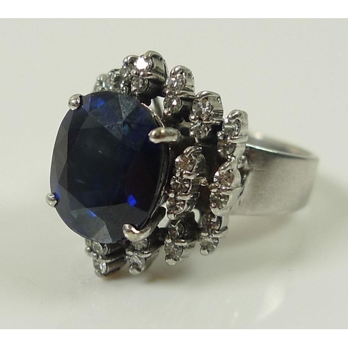 849 - An 18ct white gold, diamond and sapphire dress ring, the central oval royal blue stone of 10 by 12mm... 