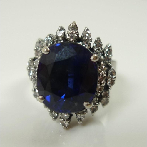 849 - An 18ct white gold, diamond and sapphire dress ring, the central oval royal blue stone of 10 by 12mm... 