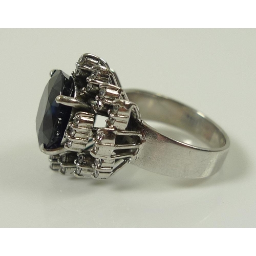 849 - An 18ct white gold, diamond and sapphire dress ring, the central oval royal blue stone of 10 by 12mm... 