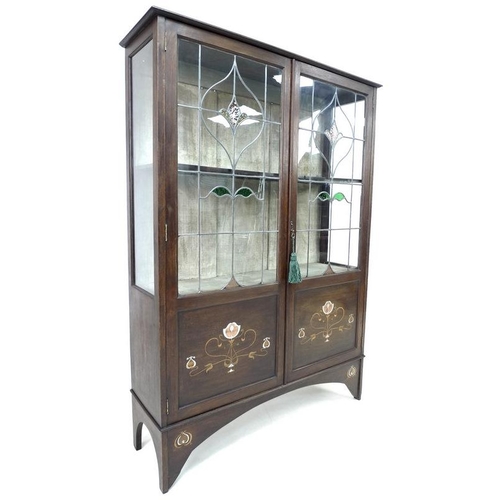 922 - An Art Nouveau mahogany, fruitwood and metal inlaid display cabinet, twin leaded stained glass doors... 