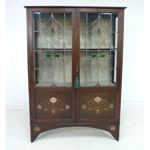 922 - An Art Nouveau mahogany, fruitwood and metal inlaid display cabinet, twin leaded stained glass doors... 