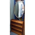 A modern mahogany freestanding bookcase, 76.5 by 20.5 by 88cm high, together with an oval wall mirro... 