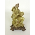 A Chinese carved figure of a smiling fisherman, possibly jade, sitting on one basket whilst holding ... 