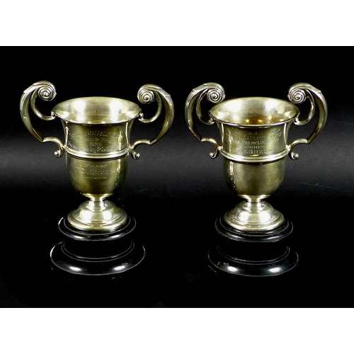 29 - A pair of silver twin handled golf trophies, flying scroll handles to knopped urnular bodies, with i... 