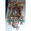 A carved wooden cuckoo clock with painted coloured foliage, with pendulum and two weights cast as pi... 